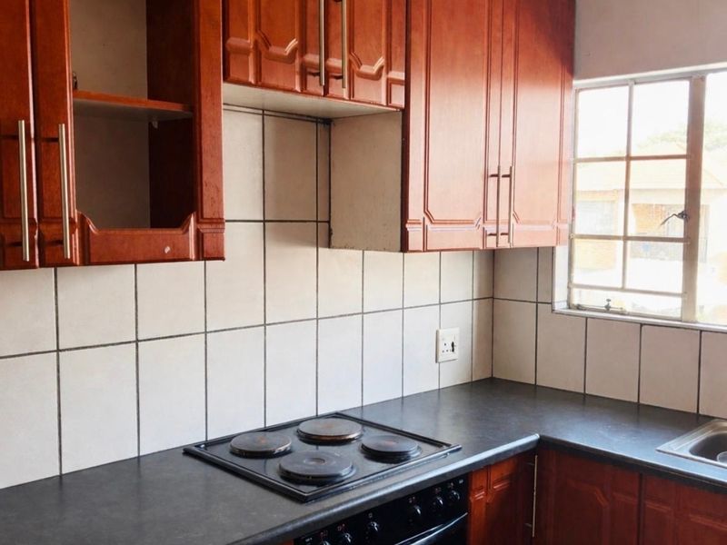 A dated kitchen featuring wooden cabinetry, a dark laminate countertop, built-in oven and hob, and a tiled backsplash.