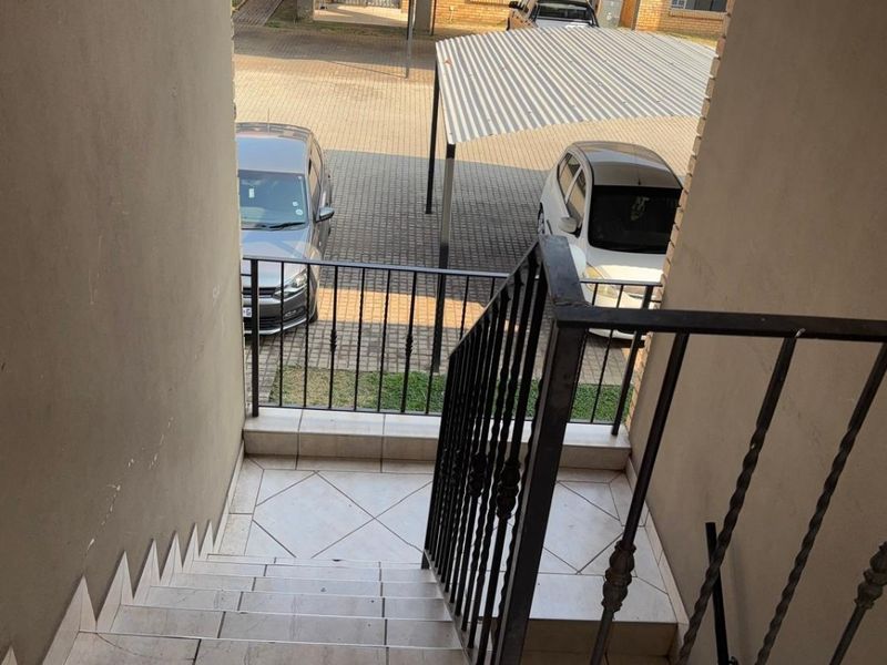 Exterior view looking down a tiled staircase towards the apartment complex parking area with metal carports.