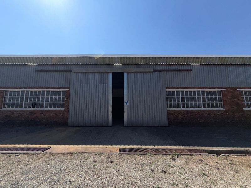 Front elevation of an industrial warehouse featuring large sliding metal doors, exposed brickwork, and steel-framed windows.
