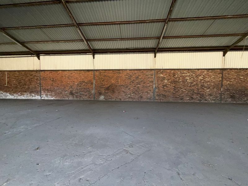 Spacious industrial utility area featuring exposed brick walls, concrete flooring, and a high corrugated metal roof with steel truss support.