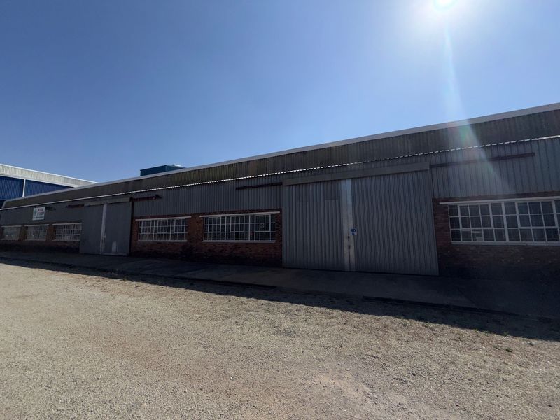 Industrial warehouse exterior featuring corrugated metal cladding, large sliding access doors, and multi-pane steel windows set above a brick base.