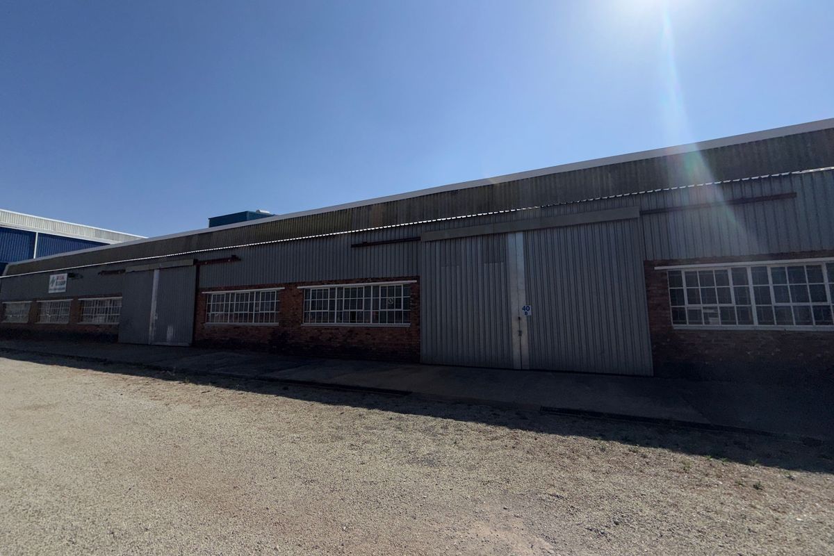 Industrial warehouse exterior featuring corrugated metal cladding, large sliding access doors, and multi-pane steel windows set above a brick base.