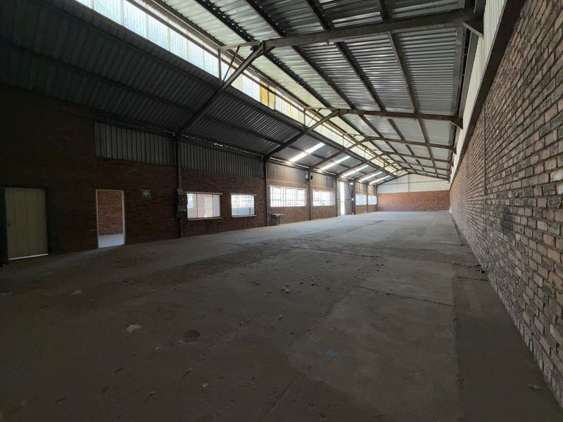 Spacious industrial warehouse unit featuring exposed brick walls, high steel truss ceilings with clerestory windows, and durable concrete flooring.
