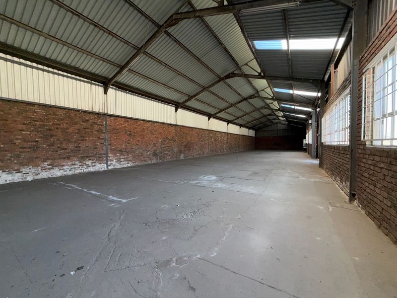 Spacious industrial warehouse unit featuring exposed brick walls, concrete flooring, steel roof trusses, and natural light provided by skylights and side windows.