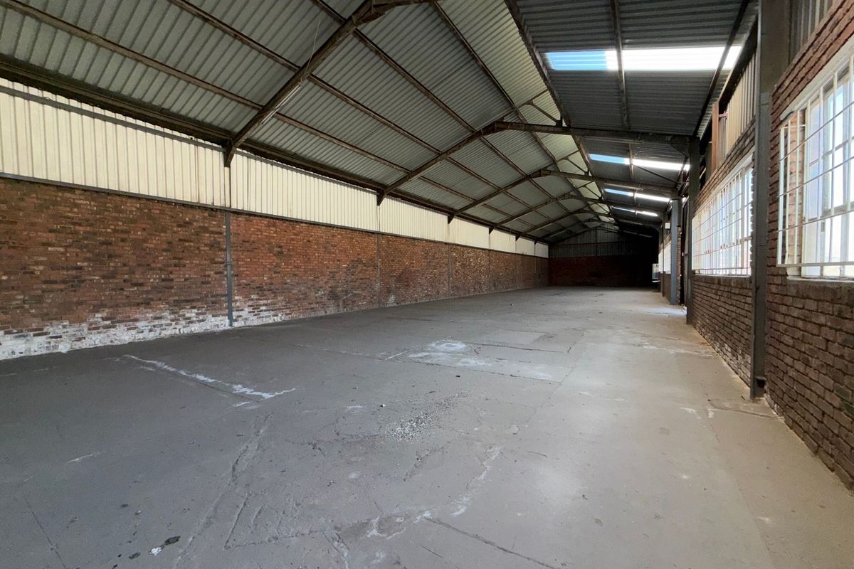 Spacious industrial warehouse unit featuring exposed brick walls, concrete flooring, steel roof trusses, and natural light provided by skylights and side windows.