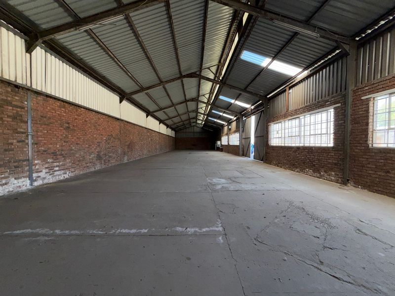 Spacious industrial warehouse unit featuring exposed brick walls, concrete flooring, steel roof structure, and natural light provided by integrated skylights and side windows.