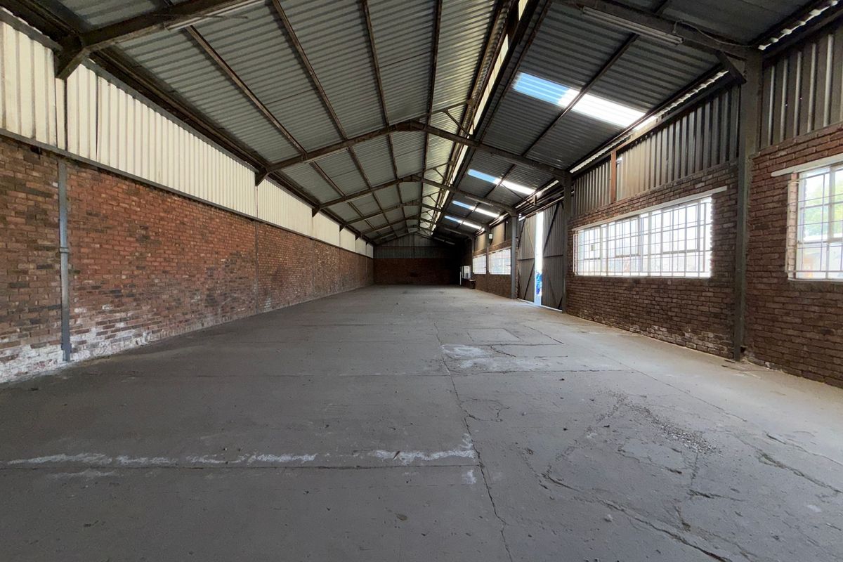 Spacious industrial warehouse unit featuring exposed brick walls, concrete flooring, steel roof structure, and natural light provided by integrated skylights and side windows.