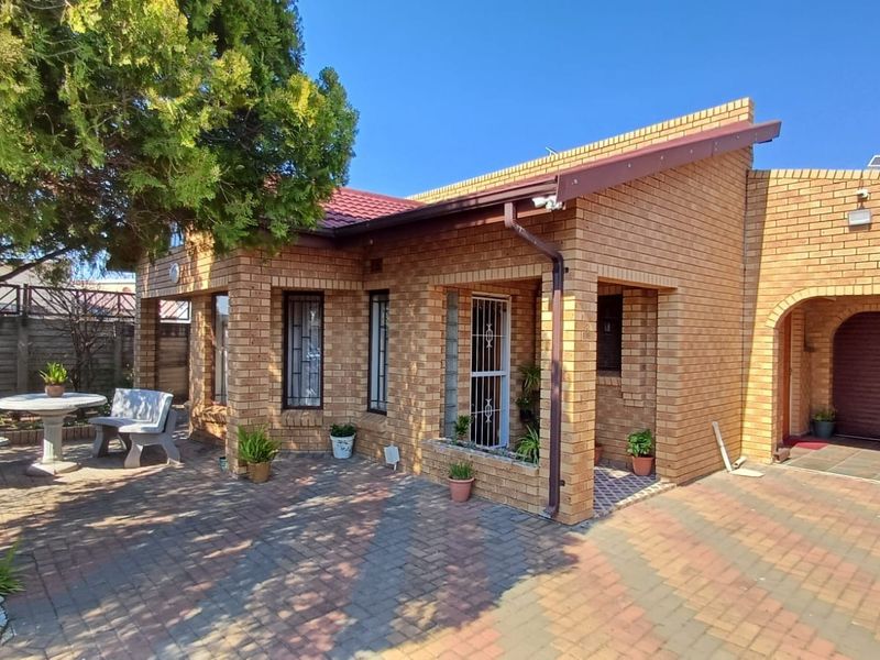 A well-maintained face brick house featuring a paved driveway, covered entrance, and an integrated garage, set within a neat residential exterior.