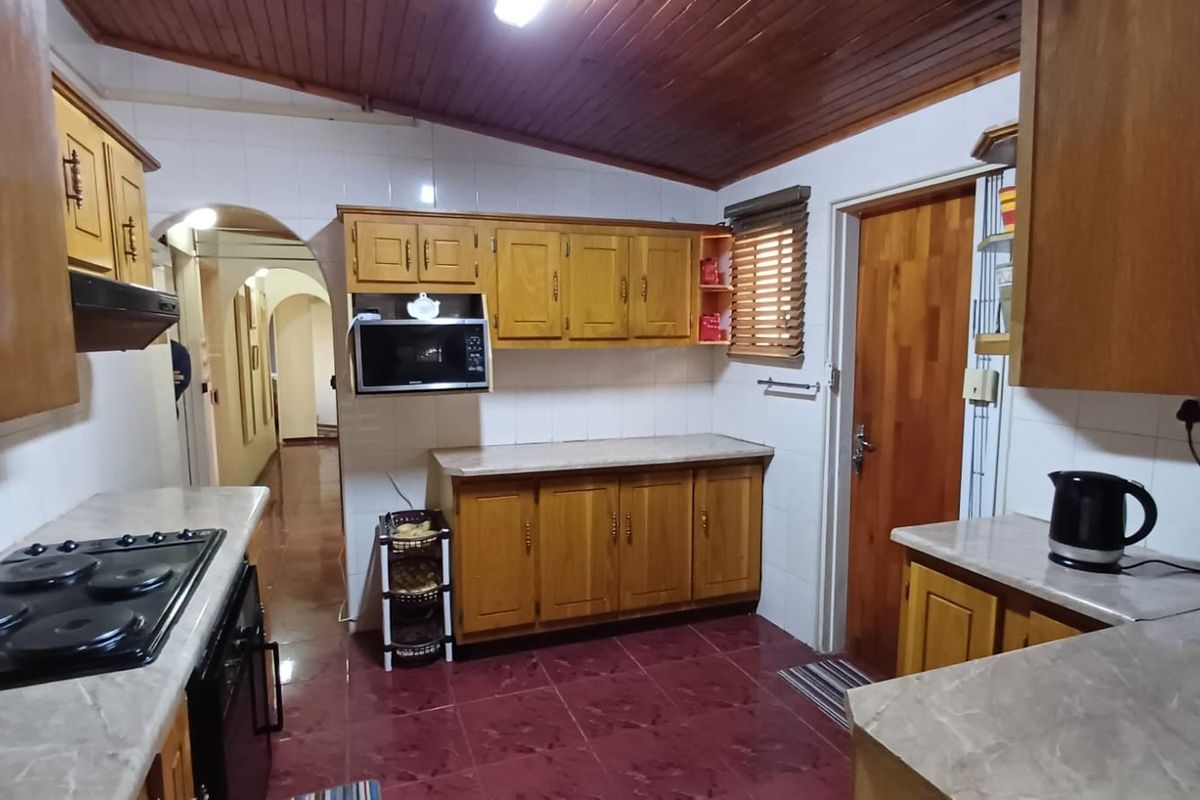 A functional kitchen featuring timber cabinetry, laminate countertops, built-in appliances, and a distinctive timber-clad ceiling with tiled flooring.