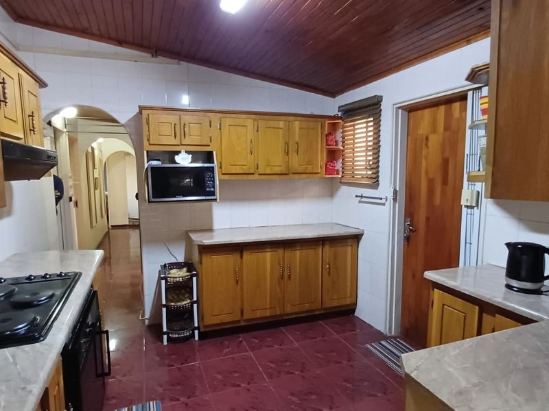 A functional kitchen featuring timber cabinetry, laminate countertops, built-in appliances, and a distinctive timber-clad ceiling with tiled flooring.