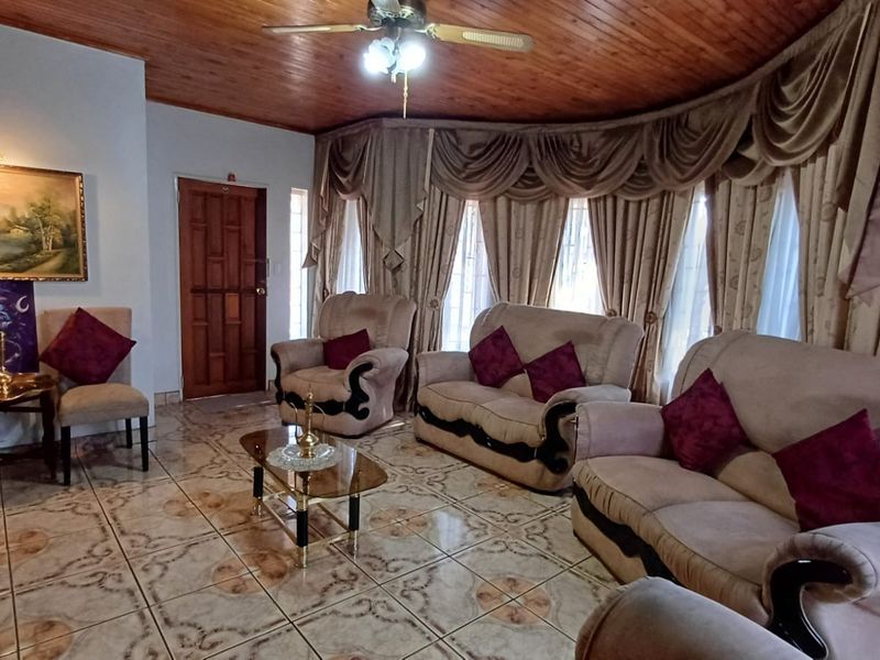 A living room featuring a timber-clad ceiling, ceramic floor tiles, and a ceiling fan, with large windows providing natural light.