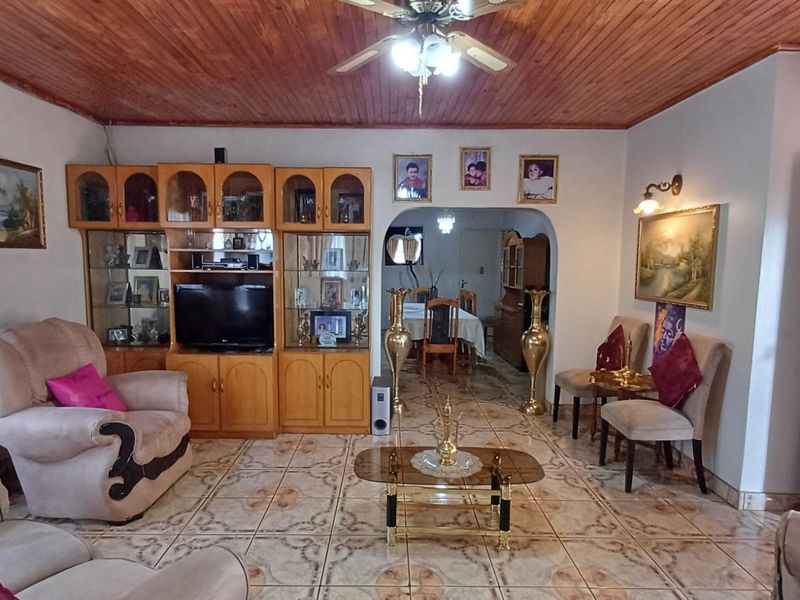 Spacious living room featuring a timber-clad ceiling, ceiling fan, tiled flooring, and built-in cabinetry, with an arched transition to the adjacent dining area.
