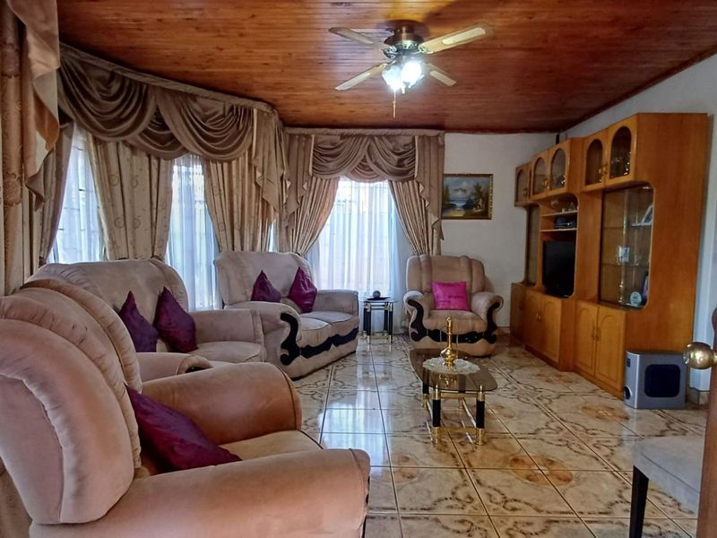 A living room featuring a timber-clad ceiling, ceiling fan, and patterned ceramic floor tiles, complemented by built-in wooden cabinetry.