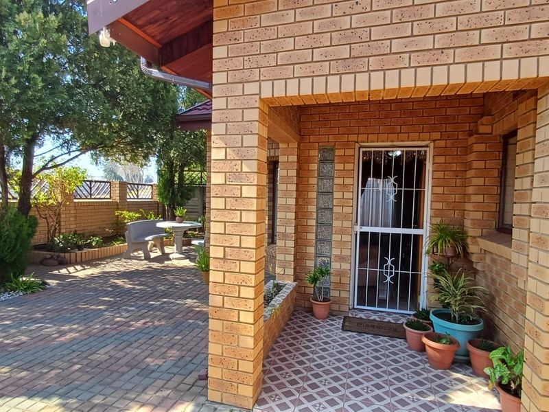 A covered patio area featuring face brick construction, paved flooring, and a secure entrance with a decorative security gate.
