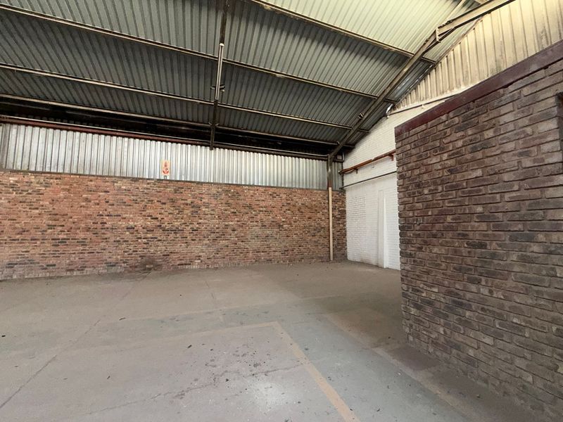 Spacious industrial utility area featuring exposed brick walls, high-clearance corrugated metal roofing, and durable concrete flooring, suitable for storage or workshop use.