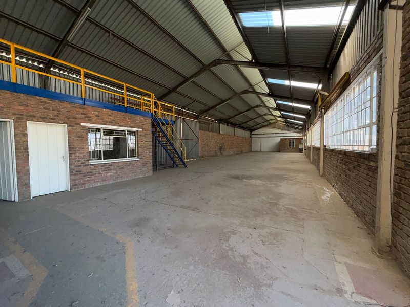 Spacious industrial warehouse featuring a mezzanine level, steel staircase, exposed brick walls, and high ceilings with integrated skylights for natural illumination.