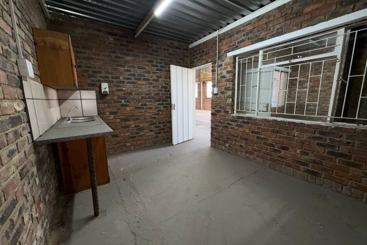 A basic industrial-style kitchenette featuring exposed brick walls, a corrugated metal ceiling, and a simple sink unit with tiled splashback.