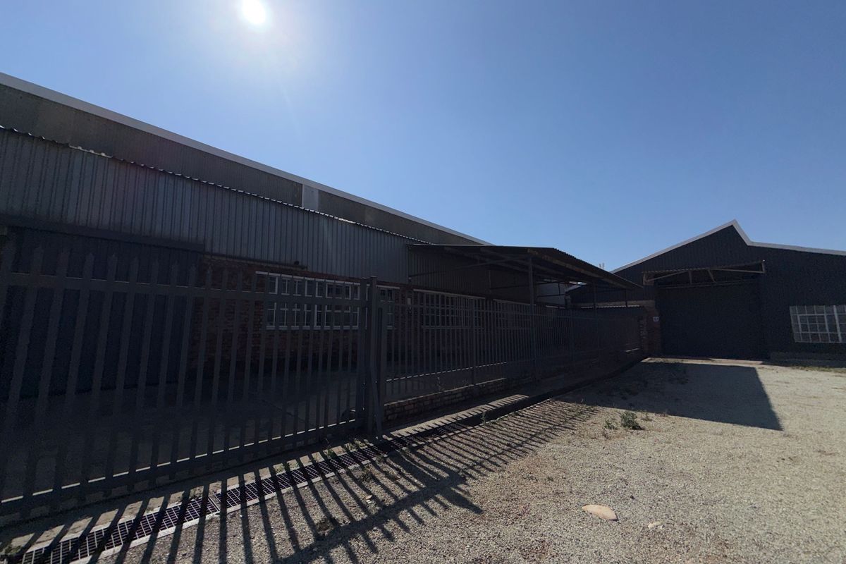 Exterior view of an industrial property featuring corrugated metal cladding, secure steel palisade fencing, and a gravel driveway area.