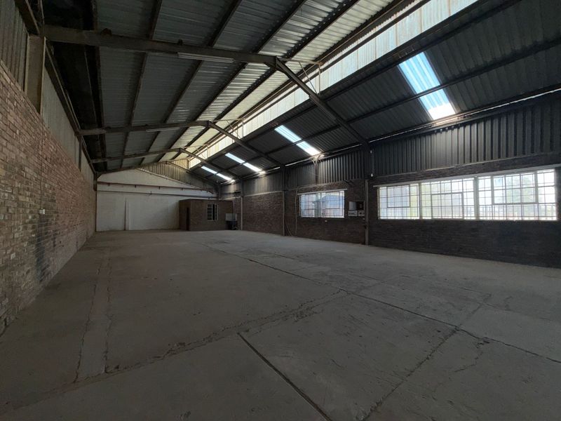 Spacious industrial warehouse unit featuring exposed steel trusses, concrete flooring, brick walls, and natural light provided by integrated skylights and large steel-framed windows.