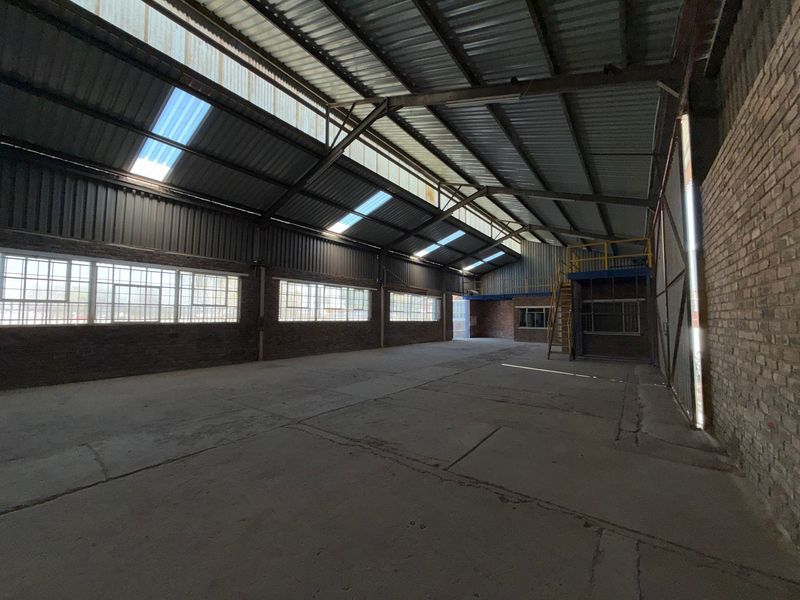 Spacious industrial warehouse featuring high ceilings with exposed steel trusses, skylights, concrete flooring, and a mezzanine level with a steel staircase.