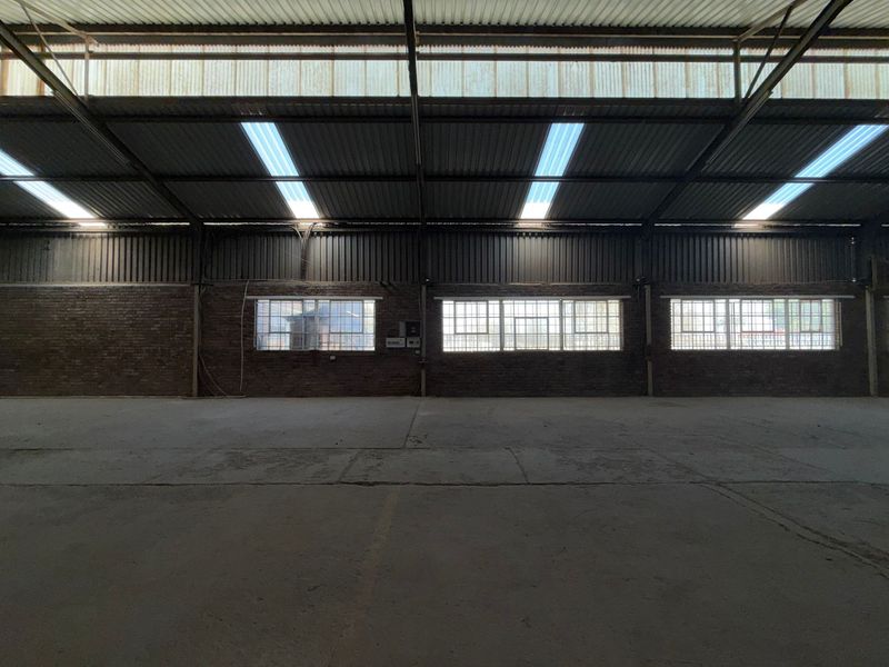 Spacious industrial warehouse unit featuring exposed brick walls, concrete flooring, high corrugated metal ceilings with integrated skylights, and secure steel-framed windows.