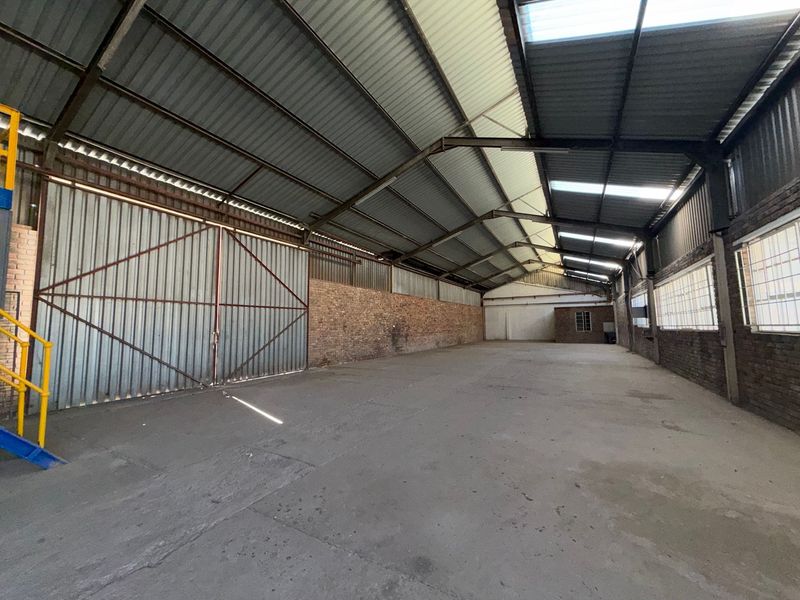 Spacious industrial warehouse featuring high ceilings with skylights, exposed brick walls, concrete flooring, and large sliding access doors.