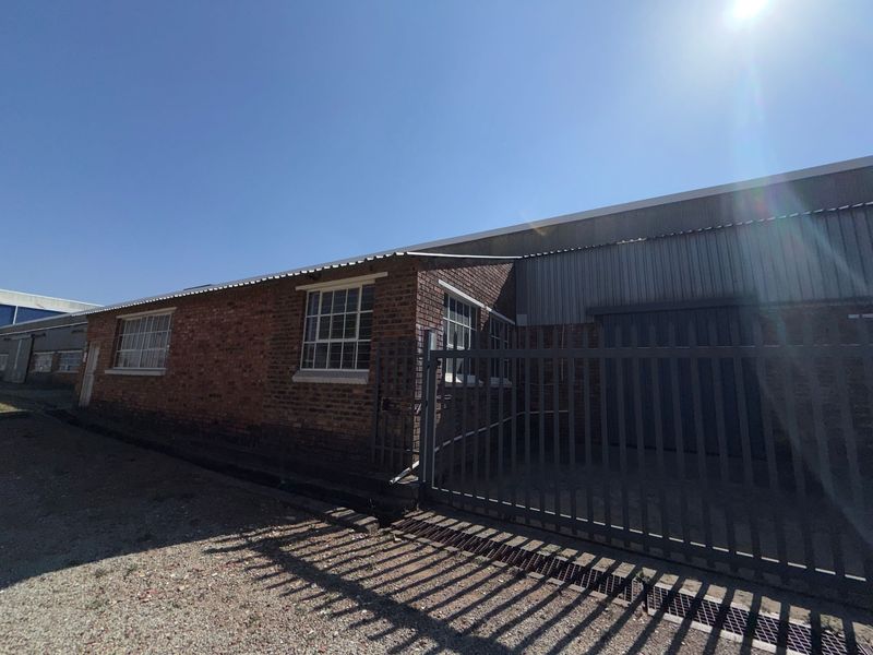 Exterior view of an industrial property featuring brick masonry, corrugated metal roofing, and a secure steel gate entrance.