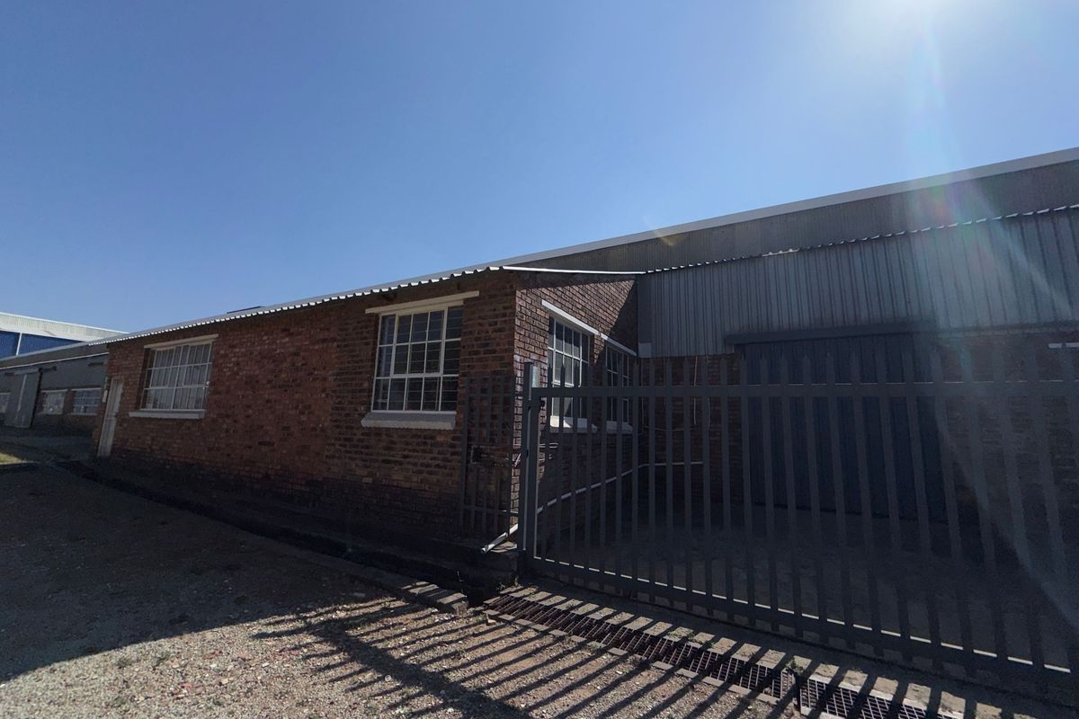 Exterior view of an industrial property featuring brick masonry, corrugated metal roofing, and a secure steel gate entrance.