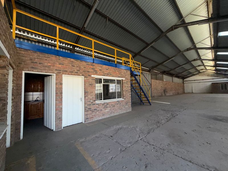 Spacious industrial warehouse featuring a mezzanine level with metal staircase, exposed brick office structure, and durable concrete flooring throughout.