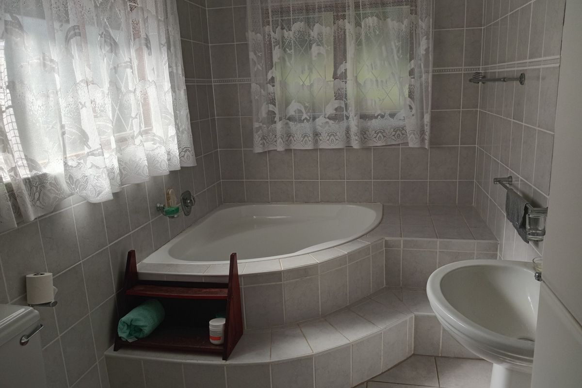 A functional bathroom featuring a corner bathtub with tiled surround, pedestal basin, and neutral wall tiling.
