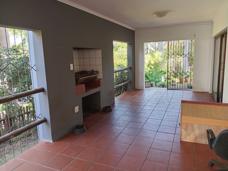 A covered patio area featuring a built-in braai, tiled flooring, and security gates, offering direct access to the garden.