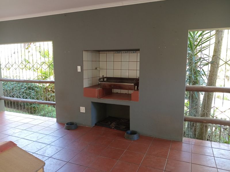 Covered patio area featuring a built-in braai, tiled flooring, and security bars, offering a functional outdoor entertainment space.