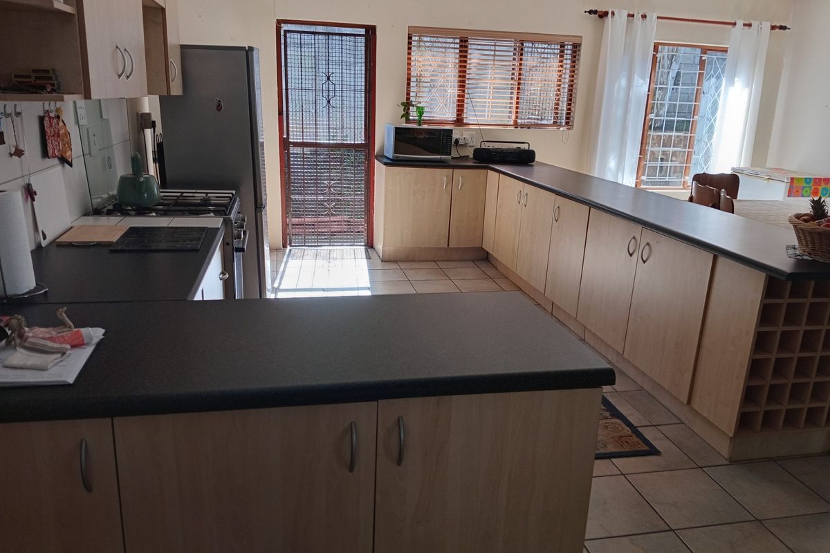 A functional kitchen featuring light wood-finish cabinetry, dark laminate countertops, a gas hob, and tiled flooring with a breakfast bar layout.