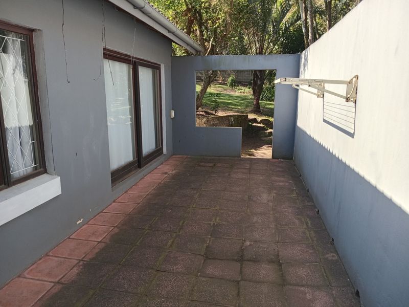 A paved outdoor patio area featuring a wall-mounted drying rack, sliding door access, and a perimeter wall with a garden view.