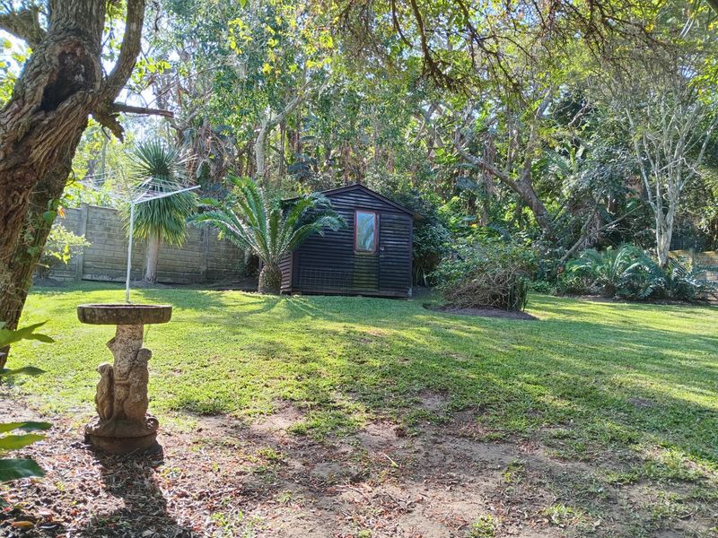 A spacious, tree-lined garden featuring a timber storage shed, concrete boundary wall, and established lawn area.