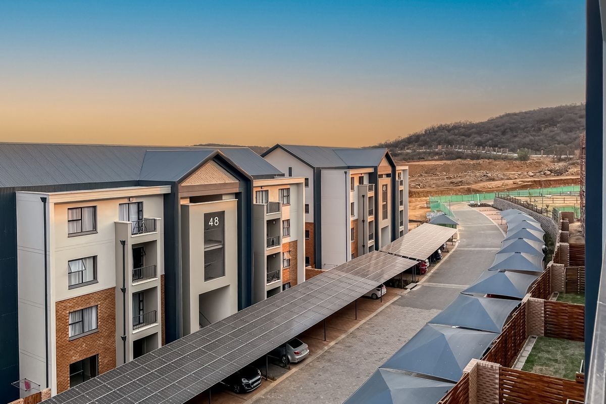 Elevated view of a modern apartment complex featuring brick and plaster facades, metal roofing, and extensive solar panel covered parking bays.