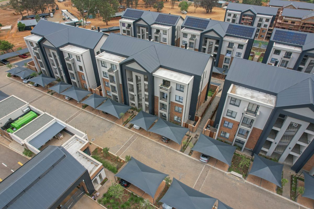 Aerial view of a modern apartment complex featuring multi-story residential buildings, paved driveways, and covered carport parking bays.