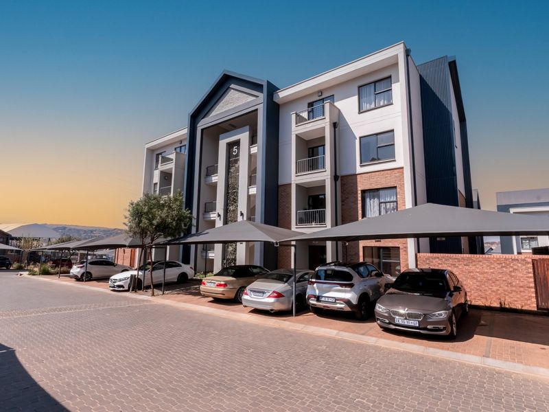 Modern apartment building exterior featuring a paved driveway, dedicated shade cloth parking bays, and private balconies with contemporary architectural finishes.