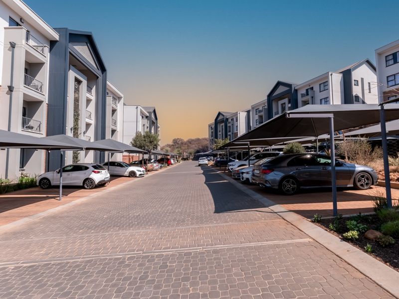 View of the apartment complex entrance featuring paved driveway and covered parking bays for residents.