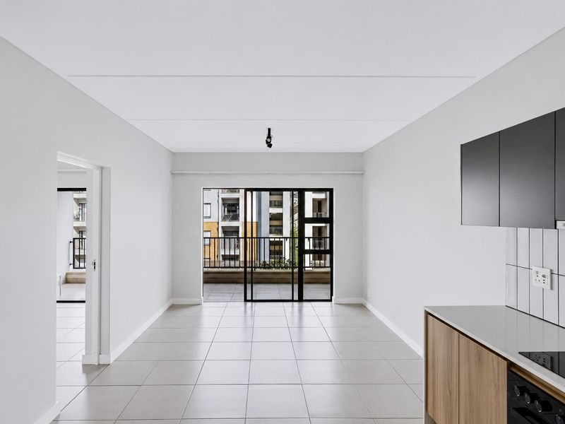 Modern open-plan living area featuring tiled floors, sleek kitchen cabinetry with built-in appliances, and direct access to a private balcony.