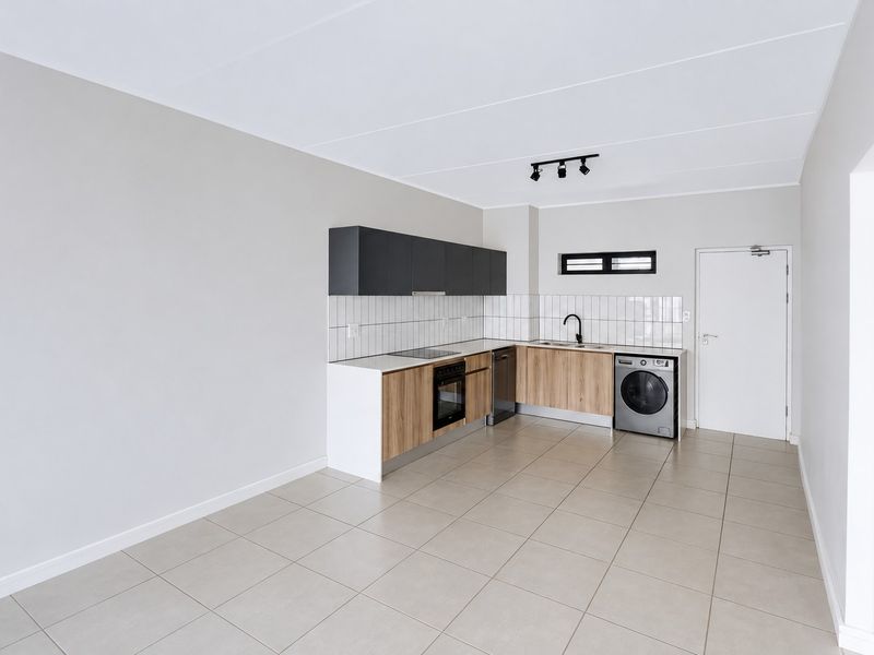 Modern, clean-lined kitchen featuring wood-finish cabinetry, dark overhead cupboards, built-in oven and hob, tiled backsplash, and neutral floor tiles in an open-plan layout.