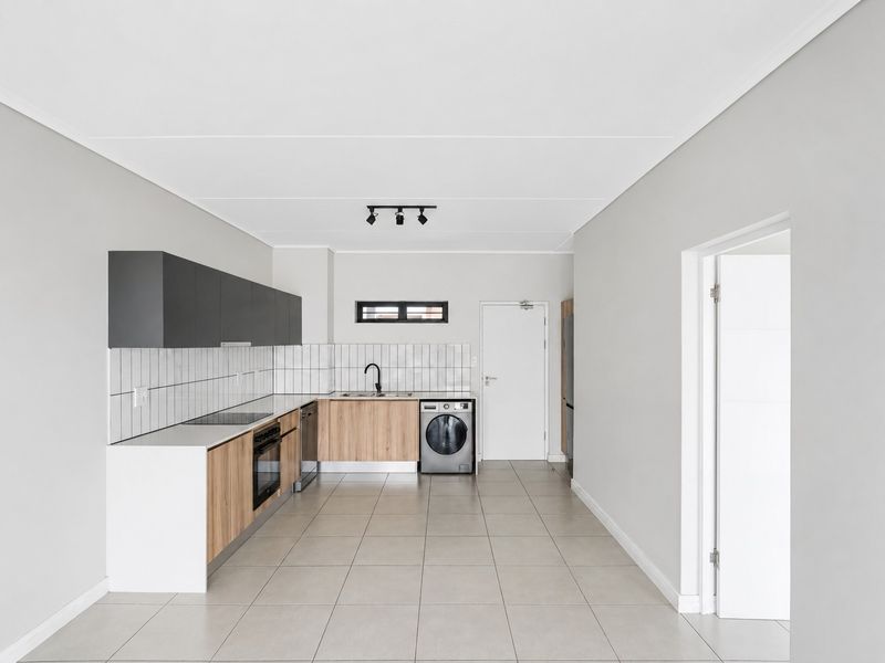 Modern, minimalist kitchen featuring wood-tone and charcoal cabinetry, integrated appliances, tiled backsplash, and neutral floor tiles in an open-plan layout.