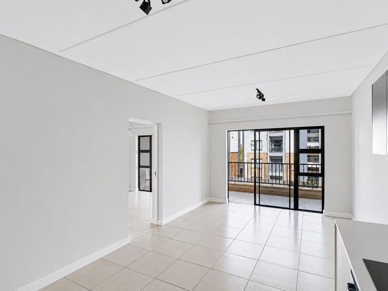 Bright and modern open-plan living area featuring neutral tiled flooring, track lighting, and direct access to a private balcony through sliding glass doors.