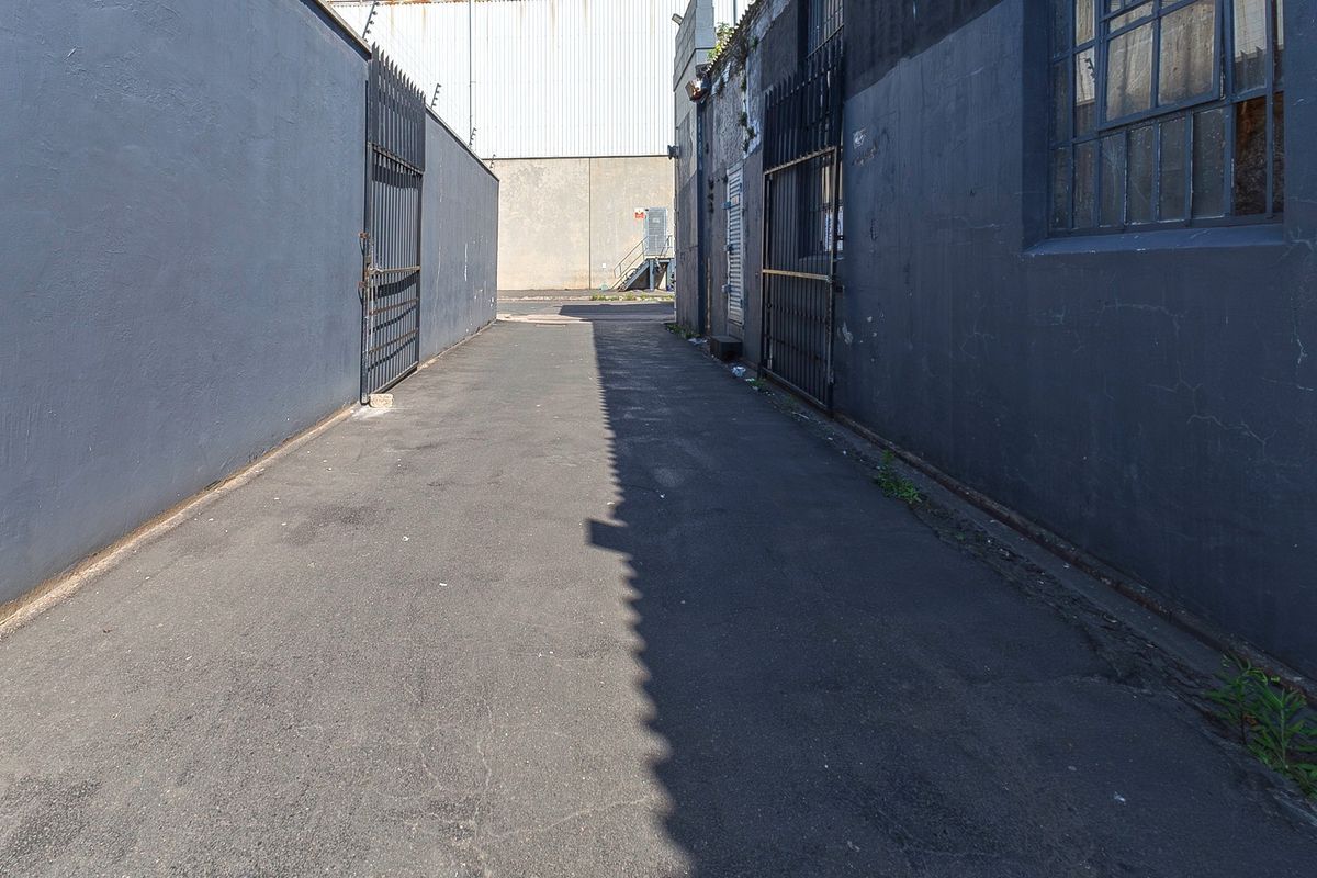 A paved rear access alleyway featuring high perimeter walls with security gates and electric fencing, providing secure service access to the commercial property.