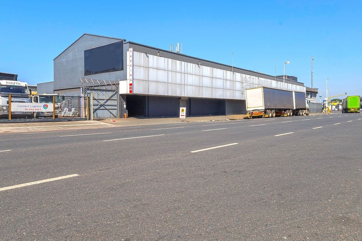Commercial industrial property featuring a large warehouse facade with metal cladding, secure gated access, and street-level parking frontage.