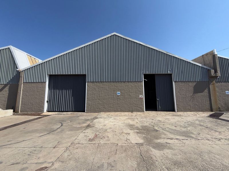 Industrial warehouse unit featuring corrugated metal cladding, masonry walls, and dual roller shutter doors with a concrete apron entrance.