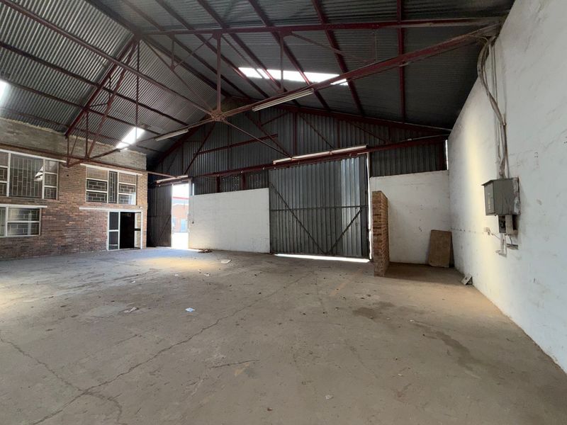 Spacious industrial warehouse unit featuring high ceilings with exposed steel trusses, concrete flooring, and large sliding access doors.