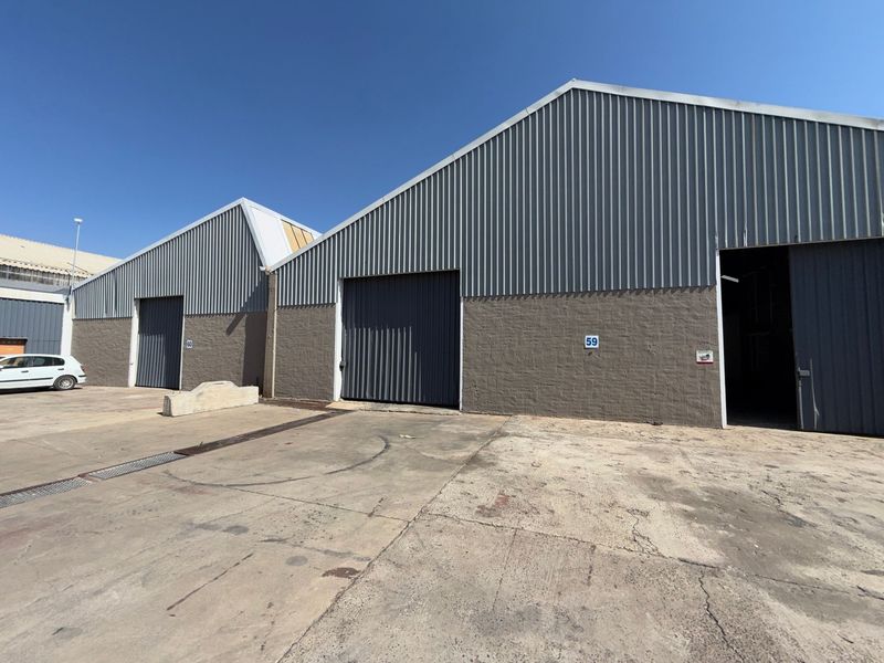 Exterior view of industrial warehouse units featuring corrugated metal cladding, large roller shutter doors, and a concrete yard area.