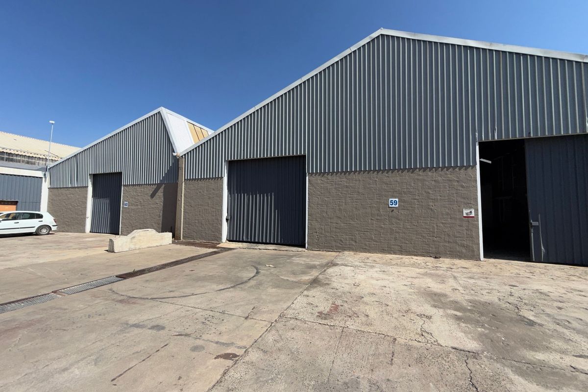 Exterior view of industrial warehouse units featuring corrugated metal cladding, large roller shutter doors, and a concrete yard area.
