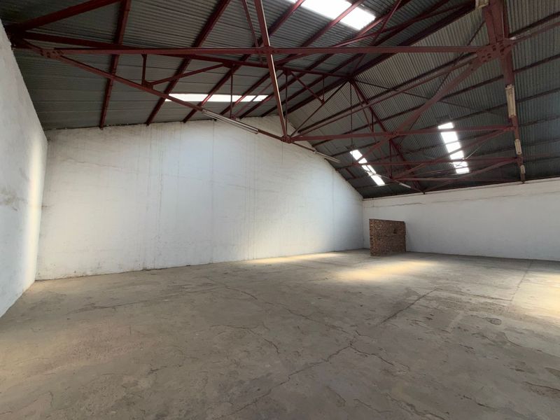 Spacious industrial warehouse unit featuring exposed steel roof trusses, natural light from skylights, and durable concrete flooring.